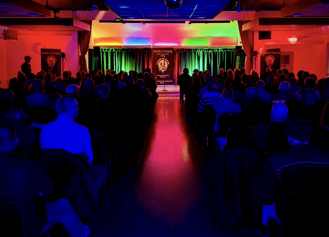 Audience facing a brightly lit comedy stage.